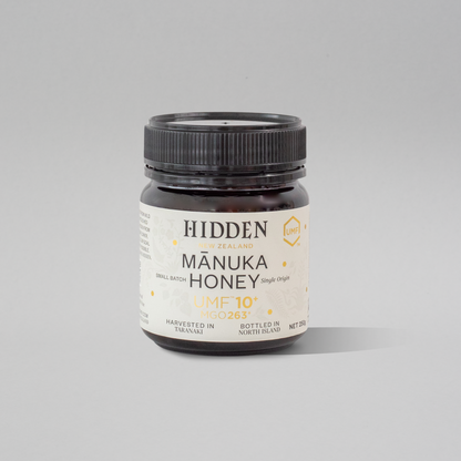 Jar of WellNest UMF10+ MGO263+ Manuka Honey in a 250g glass container, showing the honey's rich amber color.
