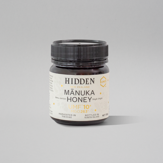 Jar of WellNest UMF10+ MGO263+ Manuka Honey in a 250g glass container, showing the honey's rich amber color.