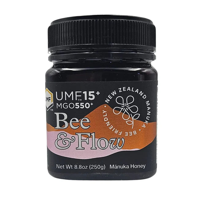 Jar of WellNest Bee & Flow Raw Manuka Honey UMF 15+ with MGO 550+ in a glass jar on a wooden surface.